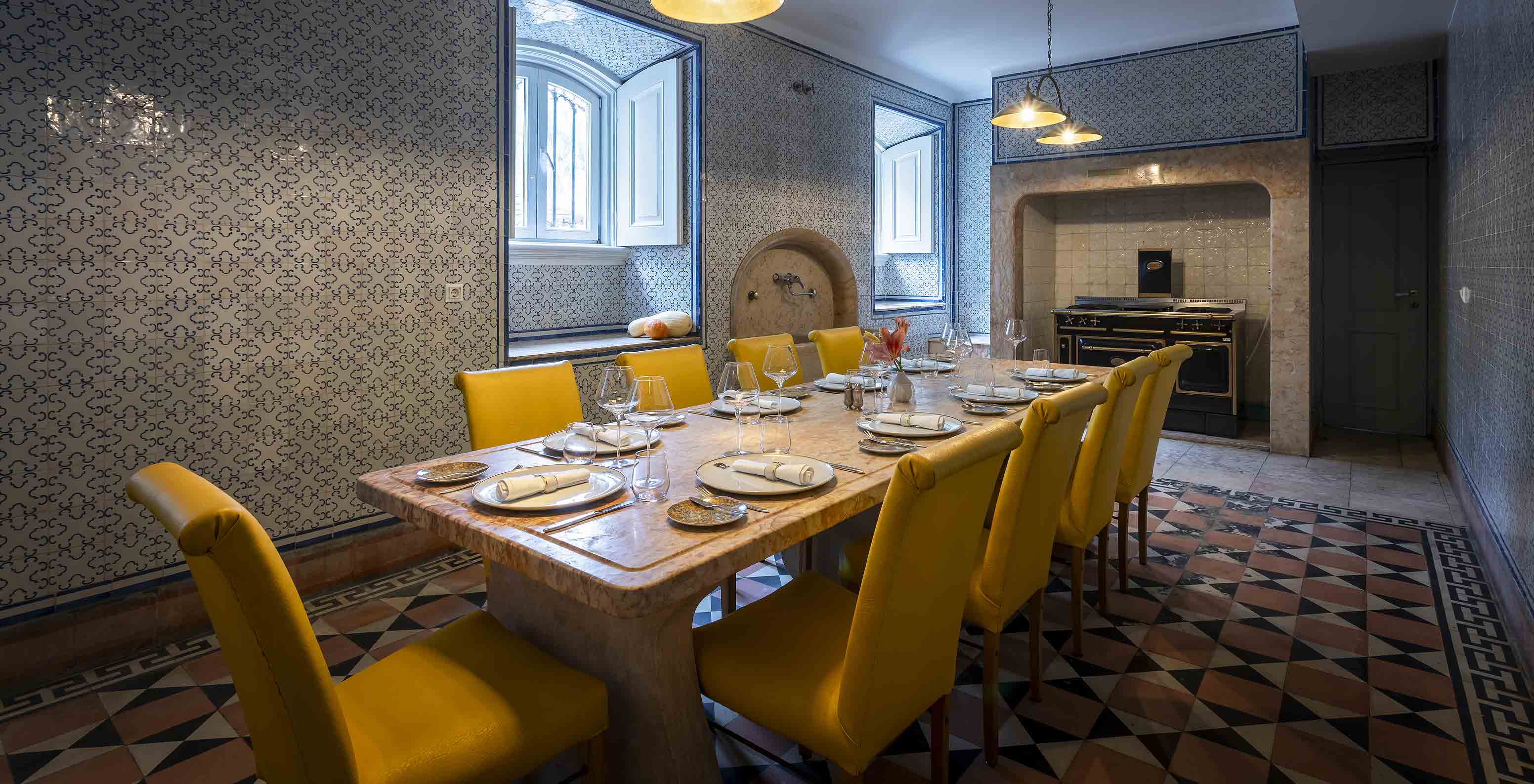 O Pestana Palace Lisboa tem uma cozinha antiga onde se fazem eventos privados com uma mesa de pedra e cadeiras amarelas 