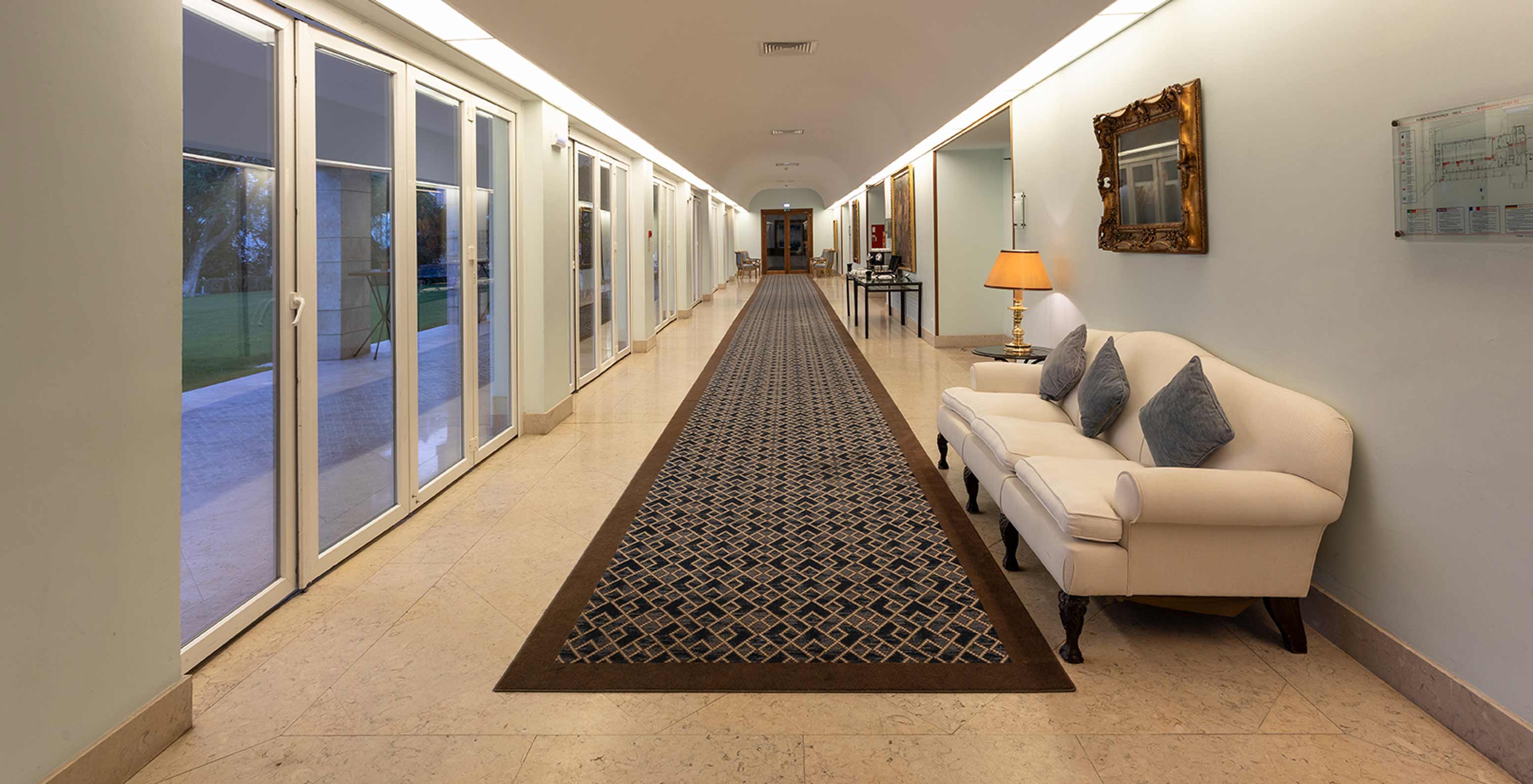 O Pestana Palace Lisboa tem um foyer com um tapete longo azul, com um sofá e grandes janelas com longos cortinados