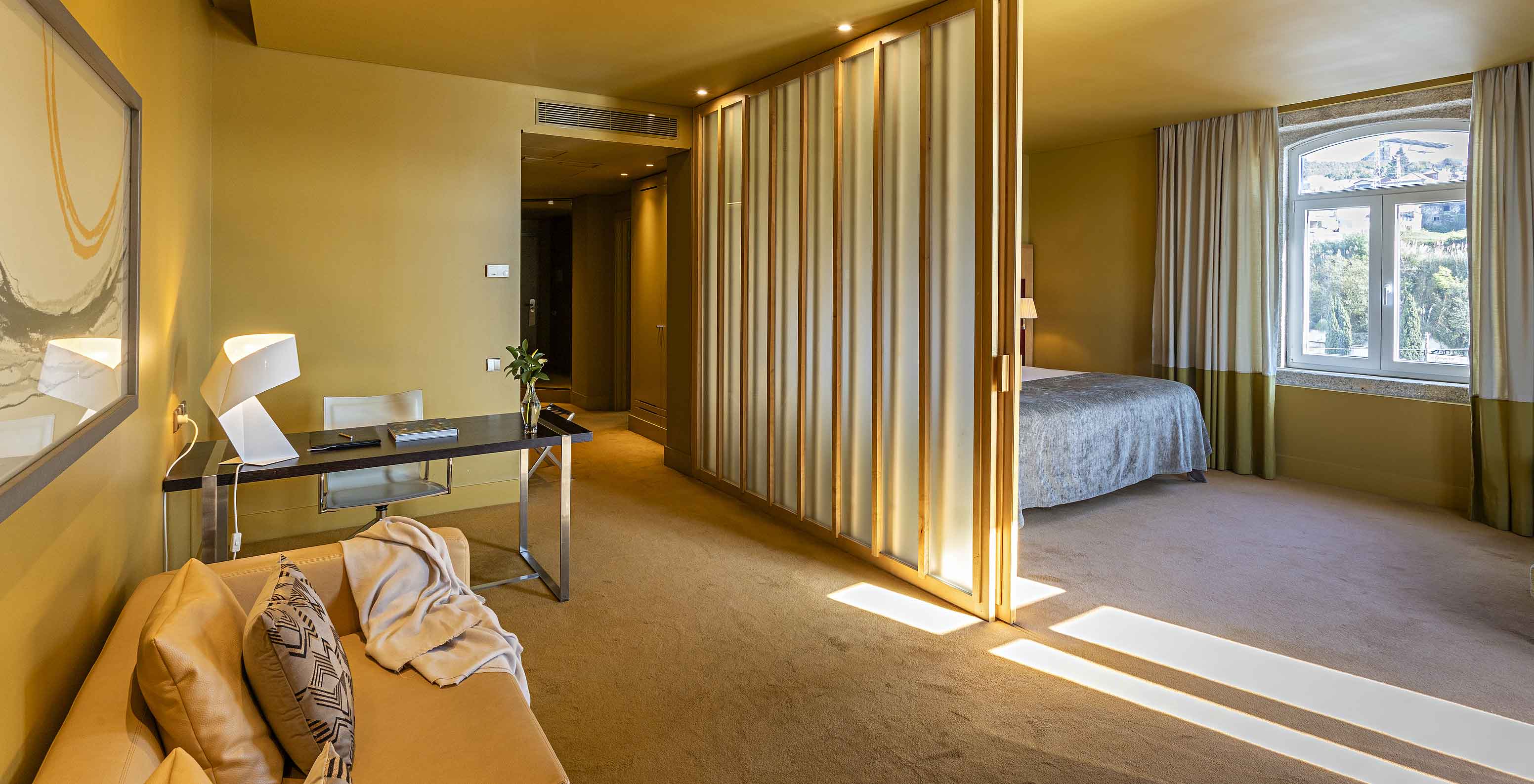 A Standard Suite do Pestana Palácio do Freixo tem uma cama de casal com uma divisória para a sala com sofá e secretária