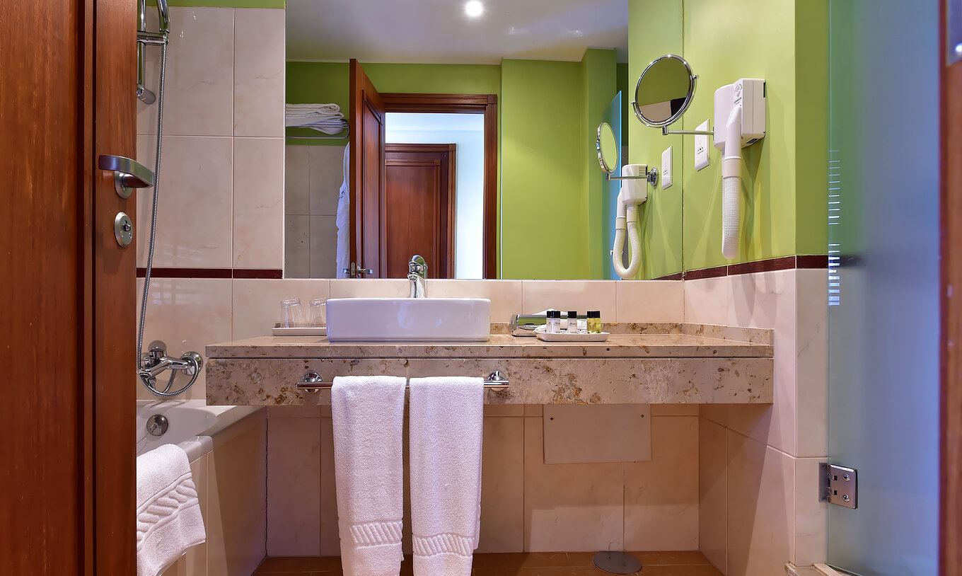 O Quarto Standard do Pestana São Tomé tem uma casa de banho com banheira com duche e uma decoração em tons neutros e verde