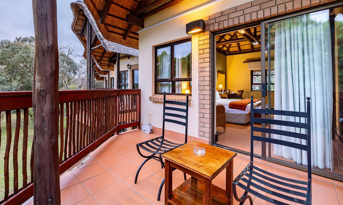 O Quarto Standard do Pestana Kruger Lodge tem uma varanda com detalhes em madeira, duas cadeiras e uma mesa de apoio