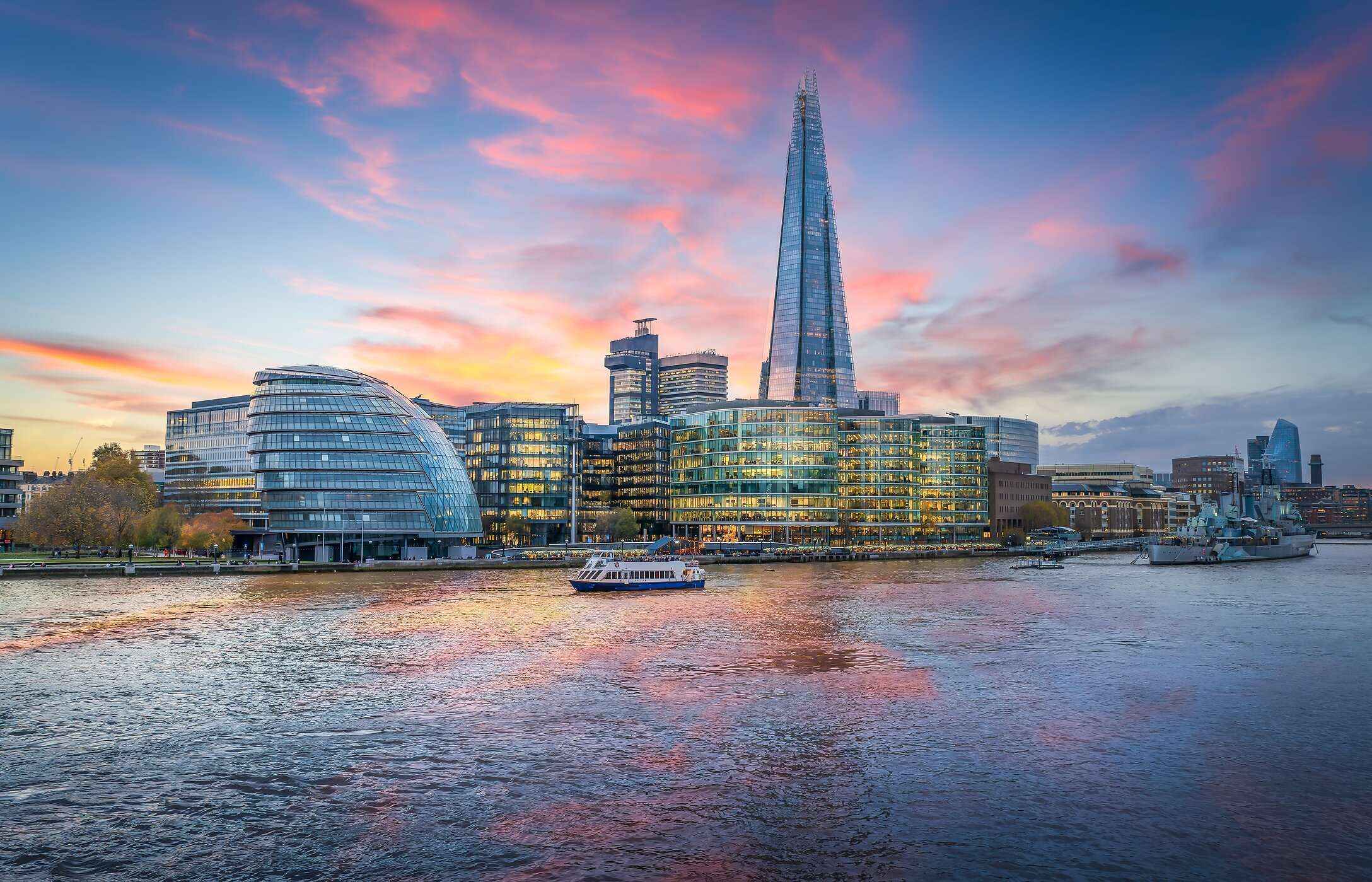 Vista panorâmica do the Shard, ao pôr do sol, com um barco a navegar no rio Tamisa, em Londres no Reino Unido