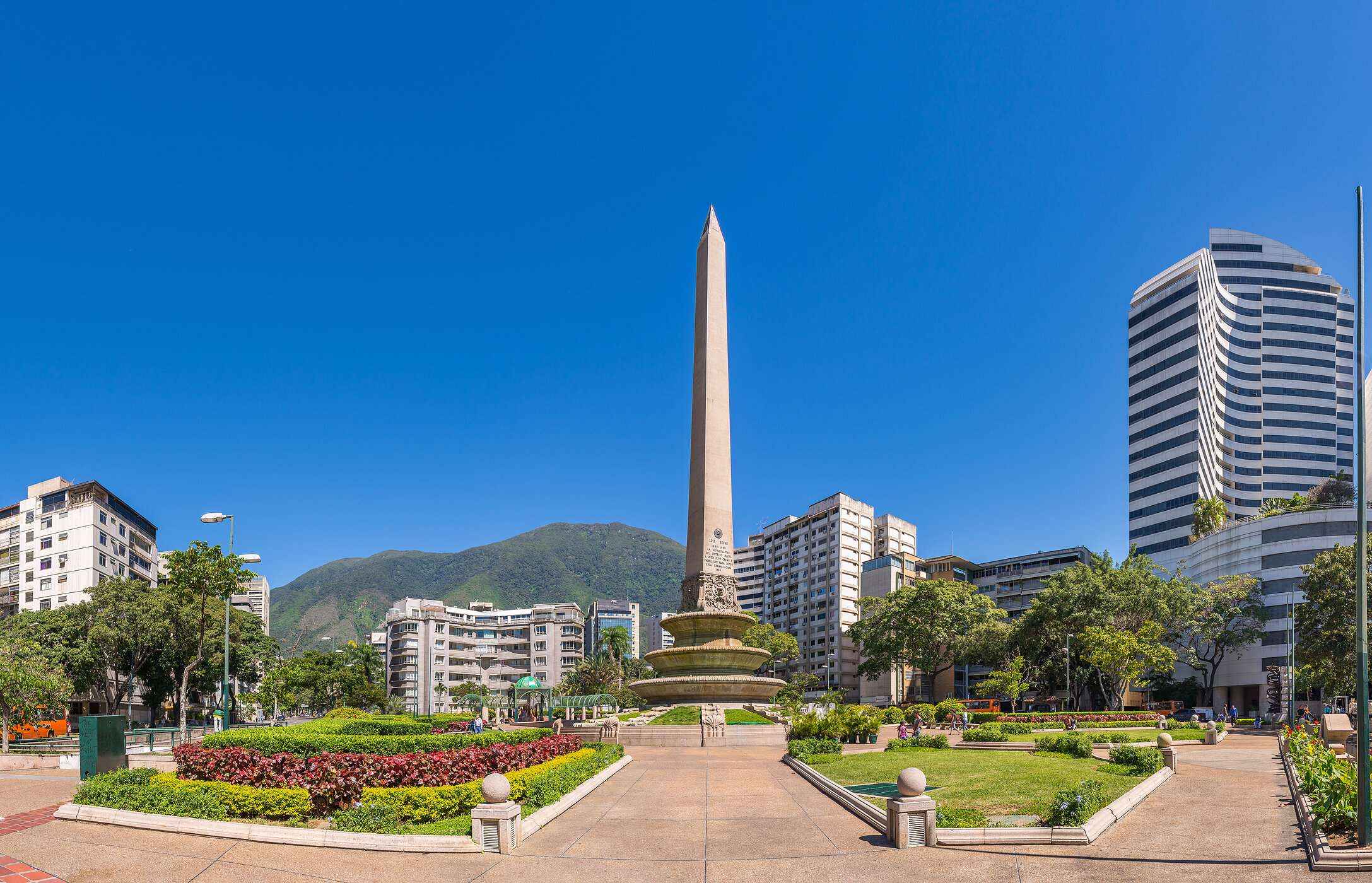 Monumento Obelisco, coluna grande de pedra no meio de um parque com flores, rodeado por edifícios altos na Venezuela