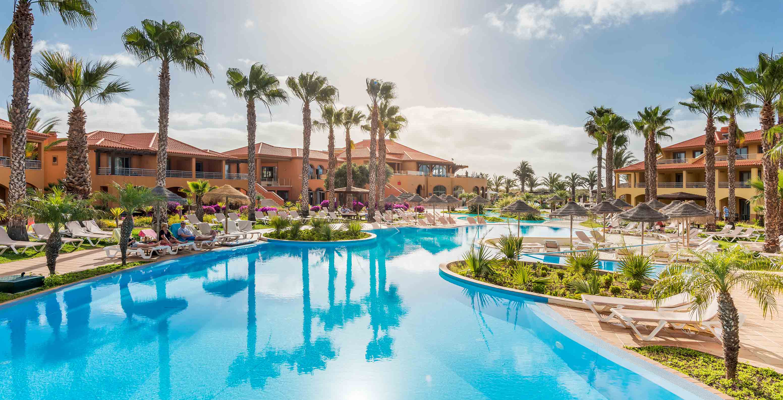 Piscina exterior com espreguiçadeiras e palmeiras no Pestana Porto Santo, Hotel com Tudo Incluído e Spa no Porto Santo