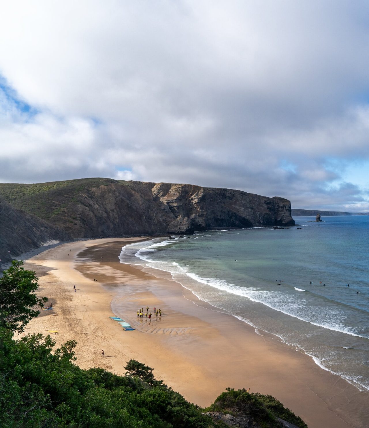 Panoramisch uitzicht op een uitgestrekt strand met rotsachtige kliffen en surfers op de golven, in de Algarve-regio