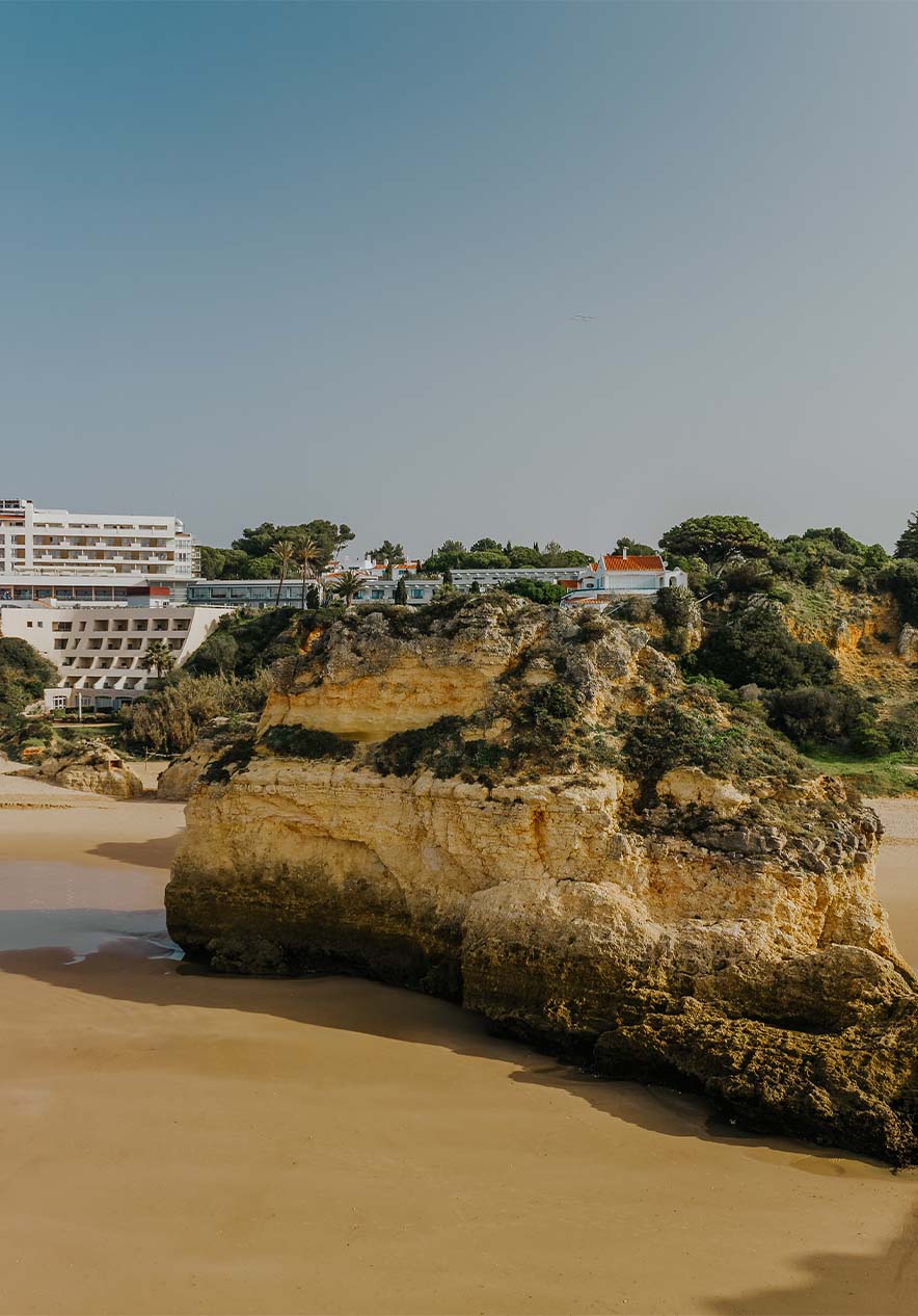 Praia do Alvor met rotsen, zand, vegetatie, de klif en gebouwen op de achtergrond, onder een heldere lucht