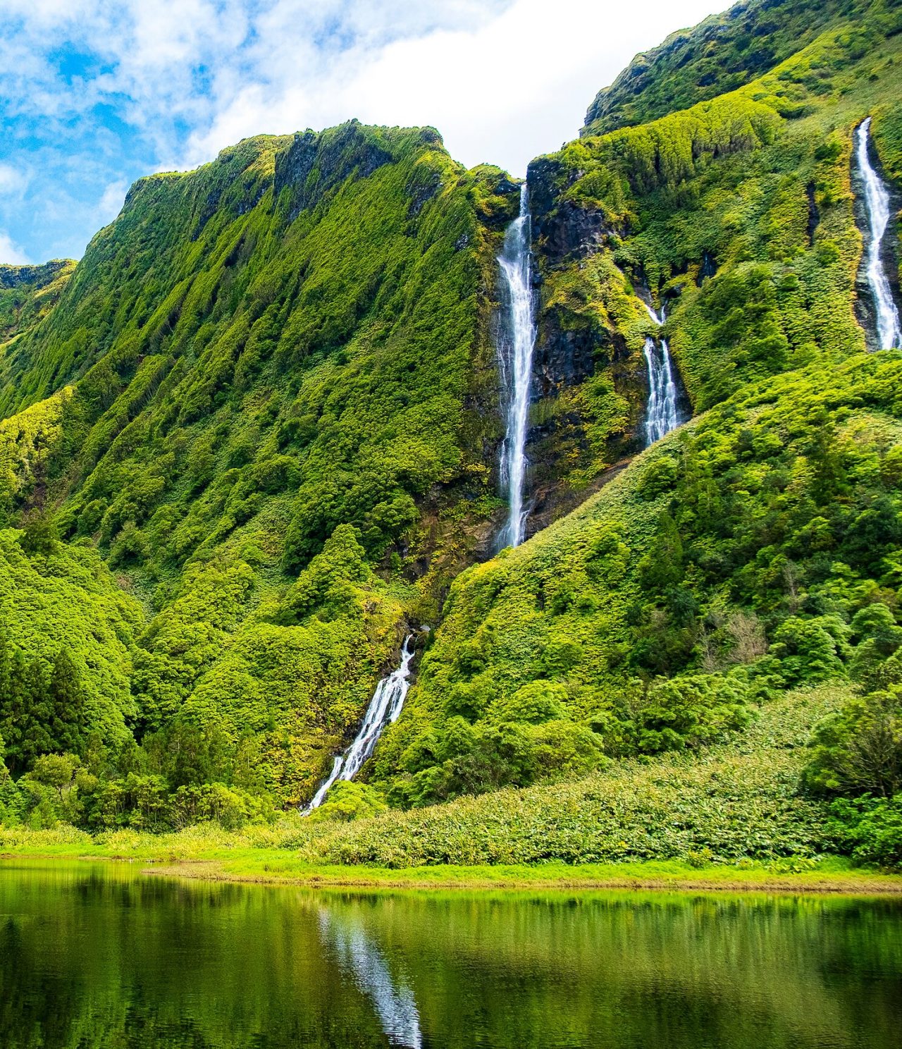 Adembenemende waterval, omgeven door met groen begroeide bergen op Flores Island, Azoren