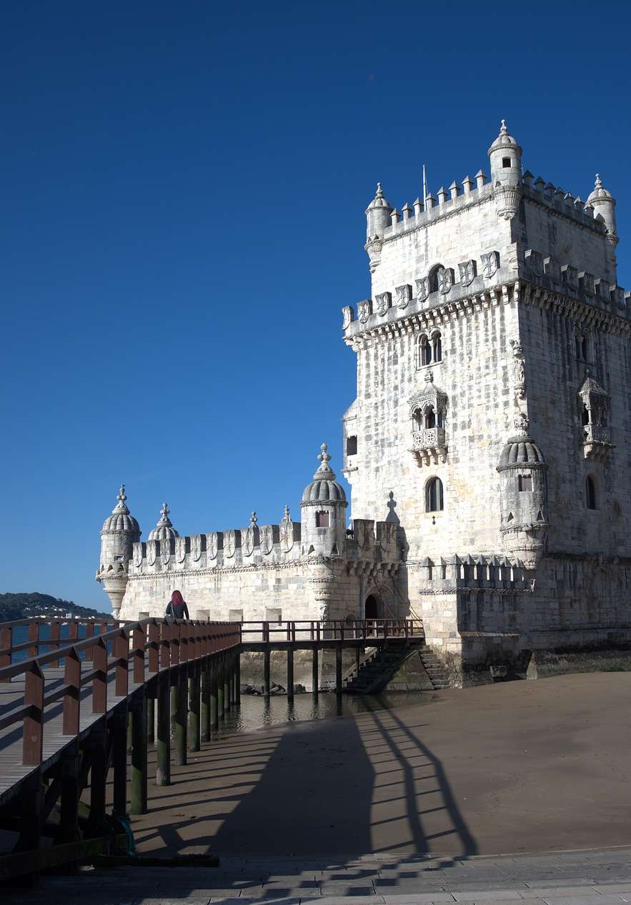 Torre de Belém, met een houten pad aan de zijkant, donker zand en de rivier de Tejo erachter