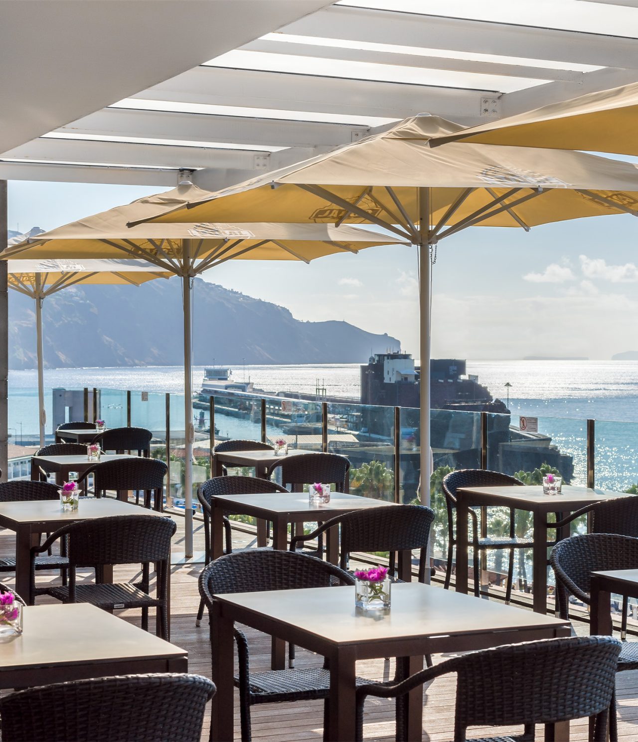 De bar Garden Pool, van het 5-sterrenhotel op Madeira, heeft een veranda met stoelen, tafels en parasols met uitzicht op zee