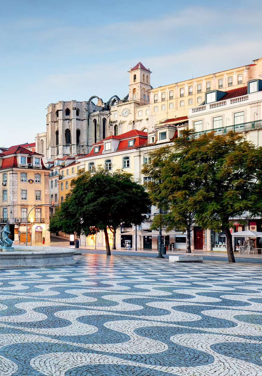 View of Rossio Square with Portuguese pavement a central fountain with statues and various buildings around