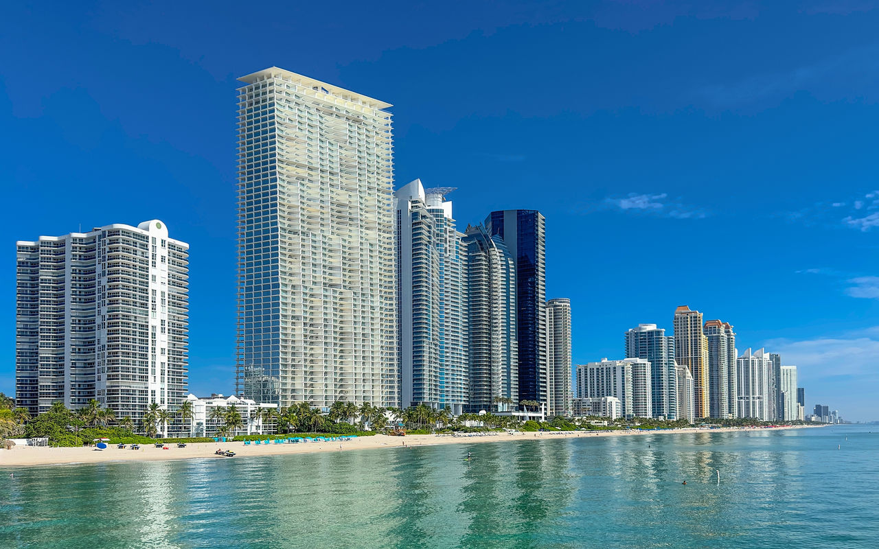 View over the coastline of Miami Beach with modern skyscrapers by the sea, light sandy beaches, and crystal blue water