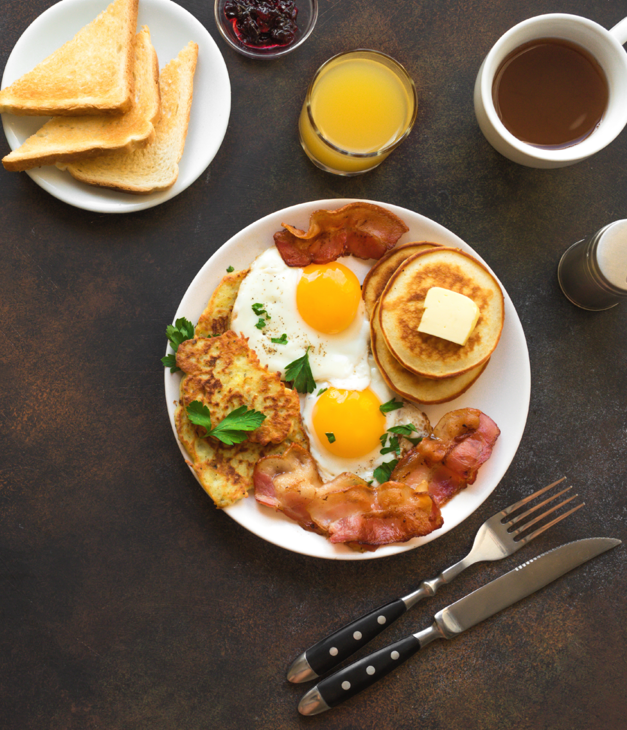 Typical American breakfast with eggs, bacon, pancakes, and toast, accompanied by orange juice and coffee