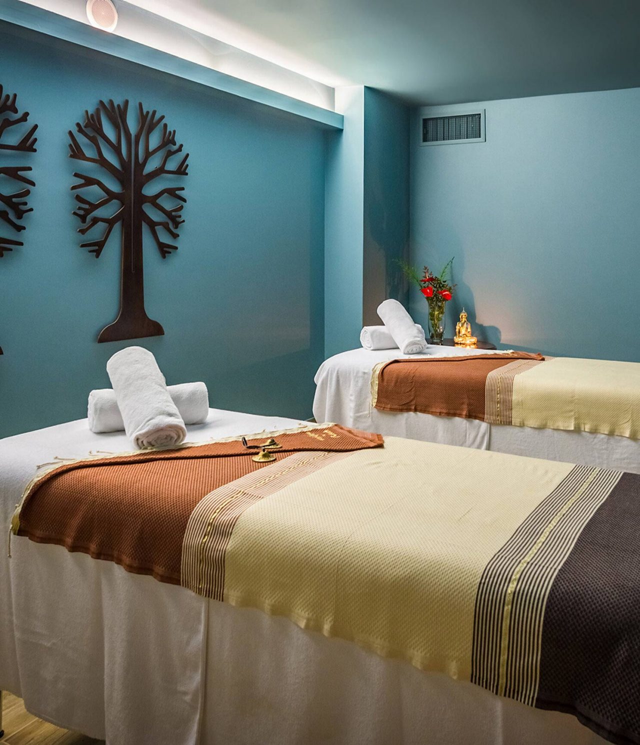 Spa room at Pestana Magic Spa, with two massage beds, artwork on the walls, and a Buddha statue on a table with flowers