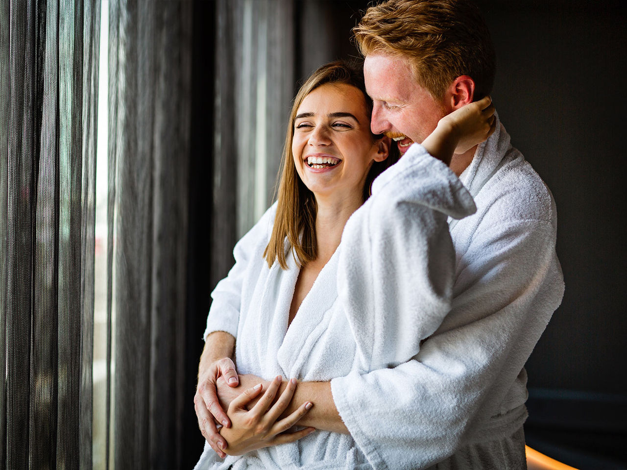A laughing couple, dressed in robes, sharing a hug and enjoying a moment of relaxation at Pestana Magic Spa