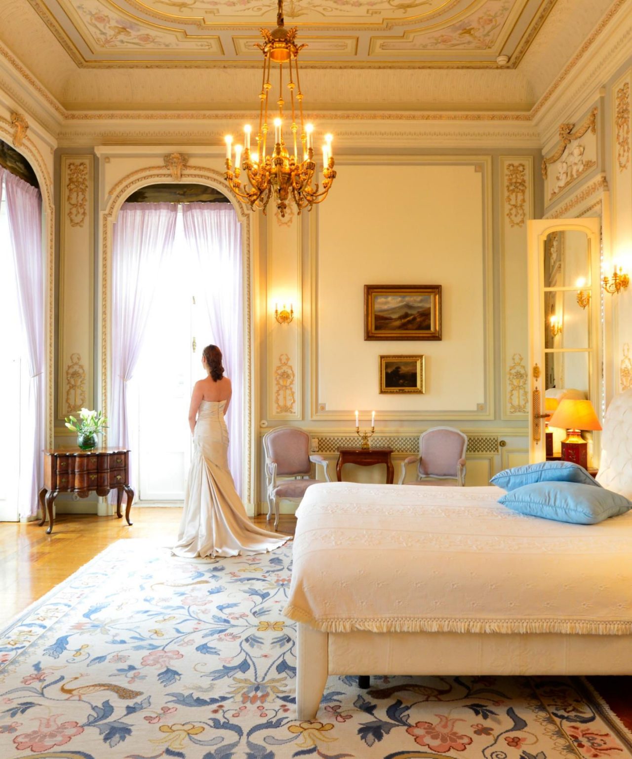 Bride prepares for her wedding in an elegant hotel room, with walls adorned with gold details and a crystal chandelier